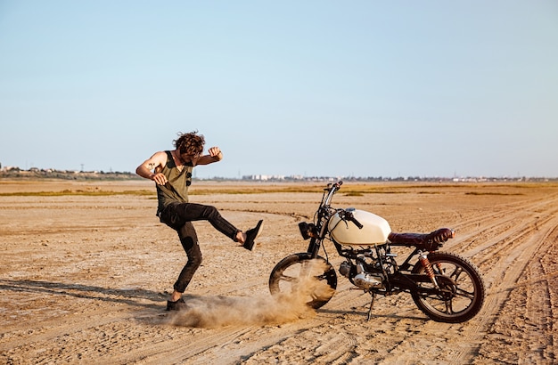 Hombre haciendo polvo de pie cerca de su motocicleta en el desierto