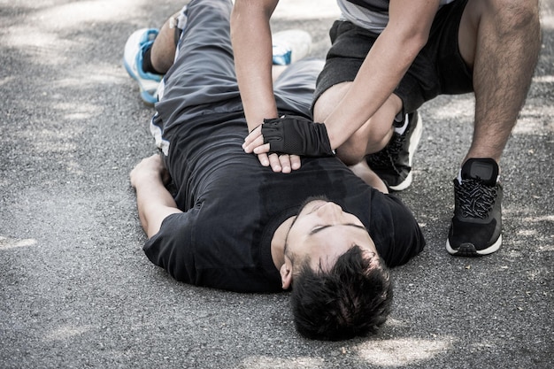 Un hombre haciendo reanimación cardiopulmonar a un tipo inconsciente después de un ataque al corazón mientras hace ejercicio en un parque