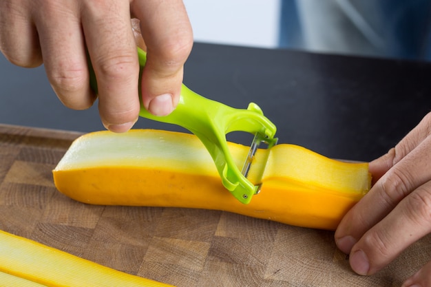 Hombre haciendo rodajas de calabacín con pelador de verduras