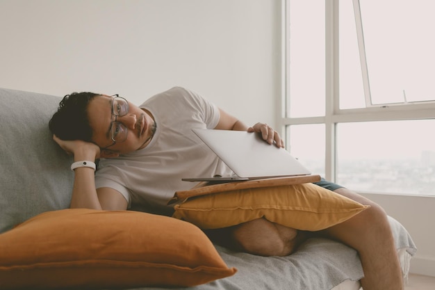 Hombre haciendo un trabajo aburrido con la computadora en su habitación sentado en el sofá