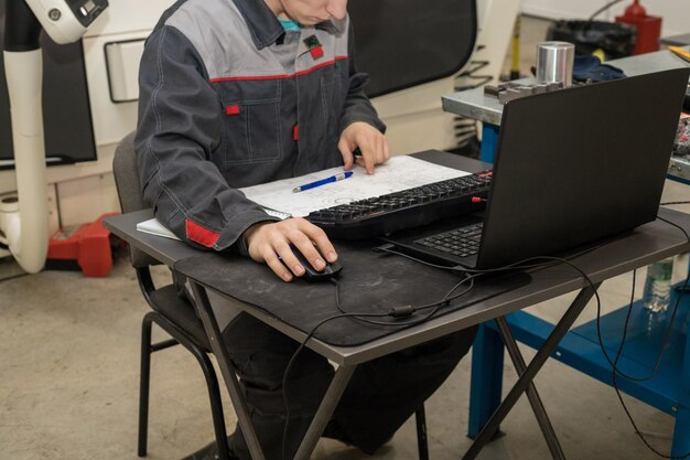 Hombre haciendo trabajo de computadora y escribiendo notas y esquemas dibujados sentado en la mesa