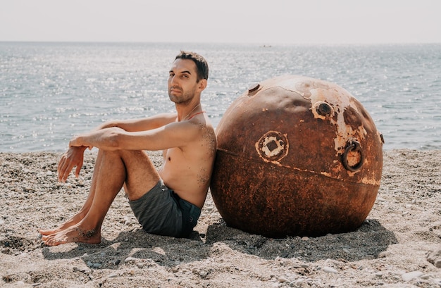 Hombre haciendo yoga y meditación al aire libre cerca de la vieja mina marina flotante oxidada en la playa con