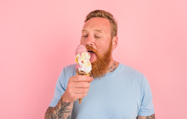 Hombre hambriento con barba y tatuajes come un gran helado