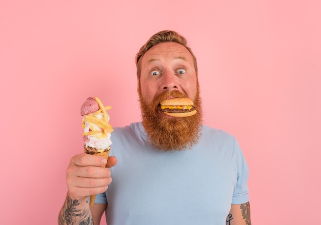 Hombre hambriento con barba y tatuajes indeciso si comer un helado o un sándwich con hamburguesa