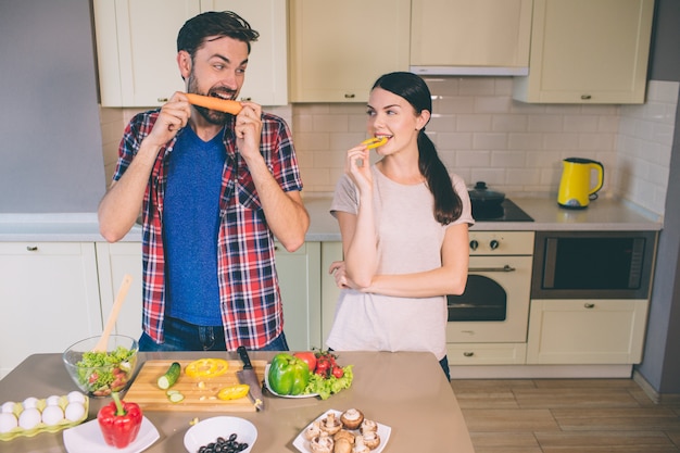 Hombre hambriento se levanta y mira a la chica. El devora la zanahoria. Chica mira vegetales.