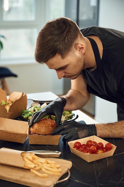 El hombre de la hamburguesa sabrosa está empaquetando comida en las cajas ecológicas de papel del restaurante interior