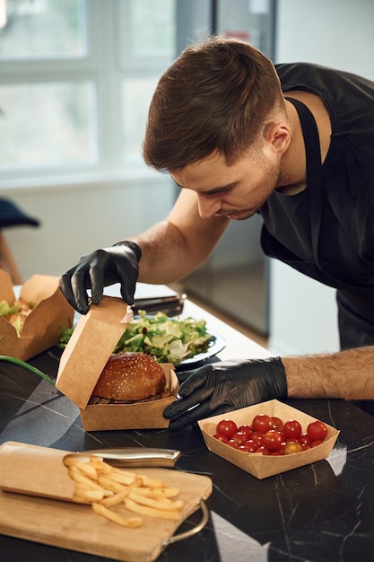 El hombre de la hamburguesa sabrosa está empaquetando comida en las cajas ecológicas de papel del restaurante interior