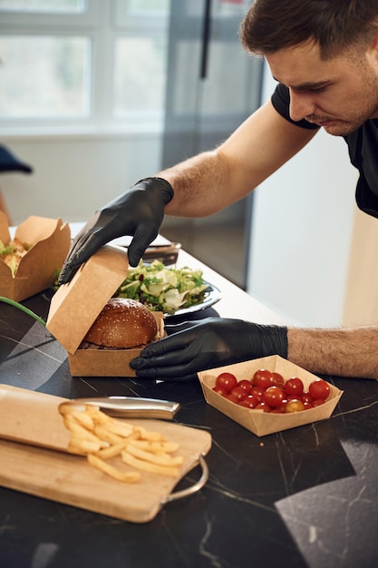 El hombre de la hamburguesa sabrosa está empaquetando comida en las cajas ecológicas de papel del restaurante interior