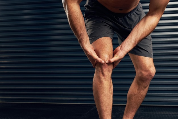 Hombre herido o atleta sosteniendo la rodilla contra un fondo oscuro para el dolor accidente o emergencia deportiva Entrenamiento persona masculina y lágrima acl para la fuerza de las piernas salud y condición física o inflamación articular