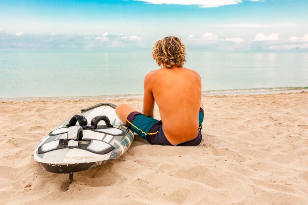 El hombre hermoso camina con la tabla de surf en blanco blanca espera la onda para surfear el lugar en la orilla del mar del océano. Concepto de deporte, fitness, libertad, felicidad, nueva vida moderna, hipster.