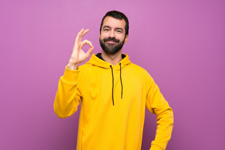 Foto hombre hermoso con la camiseta amarilla que muestra la muestra aceptable con los dedos