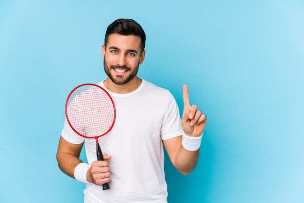 Hombre hermoso joven que juega a bádminton aislado que muestra el número uno con el dedo