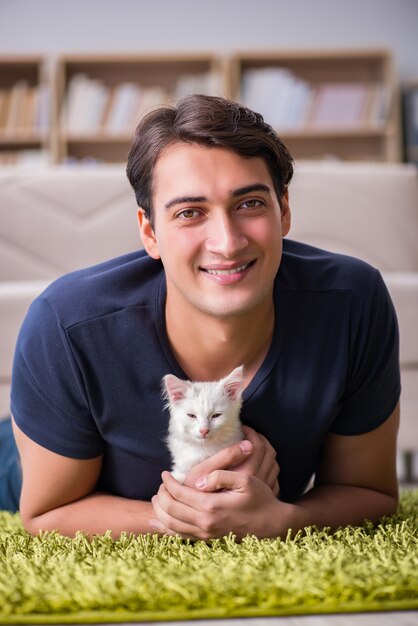 Hombre hermoso joven que juega con el gatito blanco