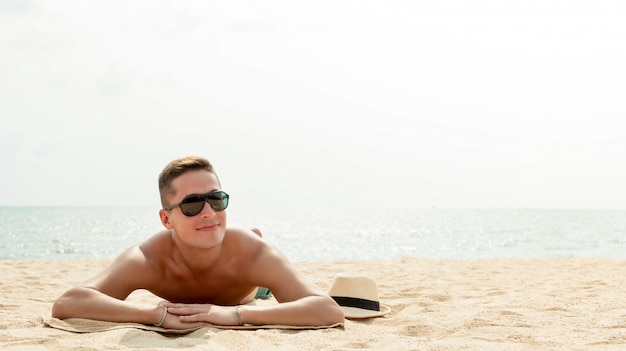 Hombre hermoso joven que miente en la playa en vacaciones de verano