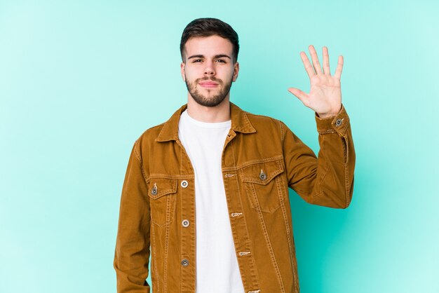 Hombre hermoso joven que sonríe alegre mostrando el número cinco con los dedos.