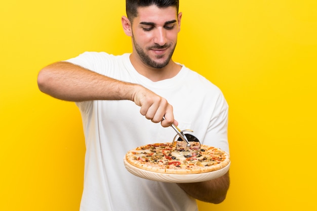 Hombre hermoso joven que sostiene una pizza sobre la pared amarilla aislada