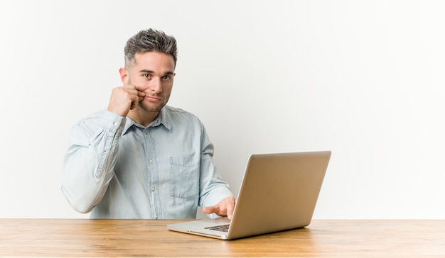 Hombre hermoso joven que trabaja con su computadora portátil con los dedos en los labios que guardan un secreto.