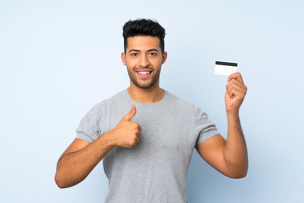Hombre hermoso joven sobre la pared aislada que sostiene una tarjeta de crédito