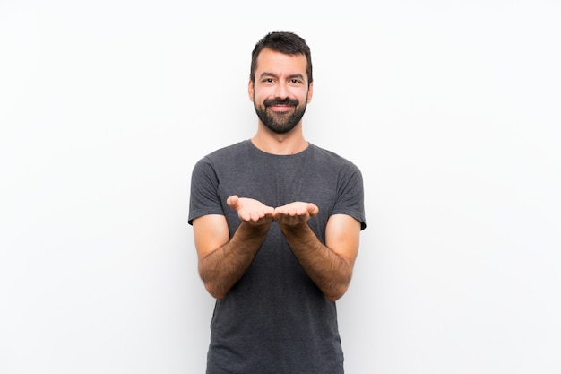 Foto hombre hermoso joven sobre la pared blanca aislada que sostiene el copyspace imaginario en la palma para insertar un anuncio