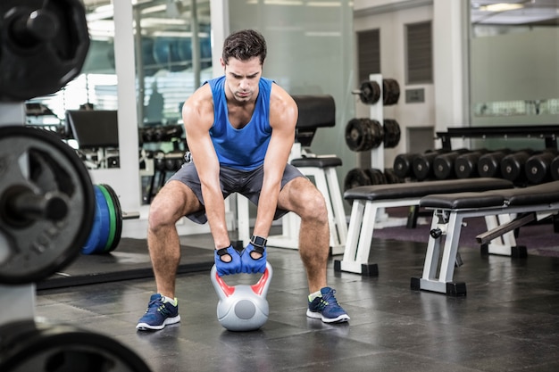 Hombre hermoso que levanta el kettlebell en el gimnasio