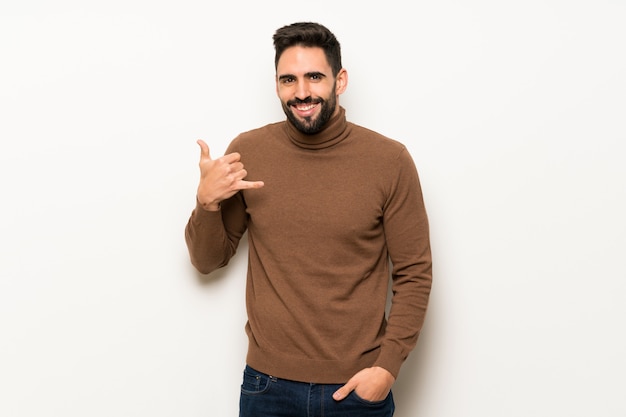 Hombre hermoso sobre la pared blanca que hace gesto del teléfono. Vuelve a llamarme señal