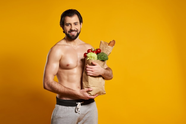 El hombre hermoso sostiene la bolsa de papel con la comida fresca.