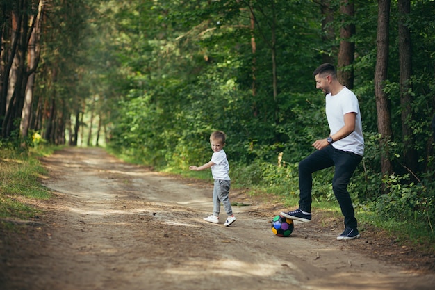 Hombre con hijo pequeño jugando al fútbol juntos cavando la pelota en el bosque pasar tiempo juntos divirtiéndose el fin de semana