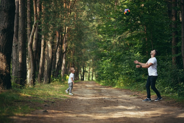 Hombre con hijo pequeño jugando al fútbol juntos cavando la pelota en el bosque pasar tiempo juntos divirtiéndose el fin de semana