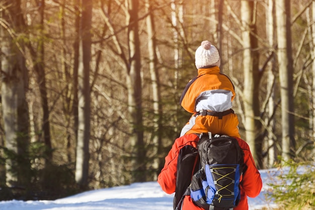 Hombre con hijo sobre los hombros caminando por la carretera en un bosque nevado Primer día de invierno