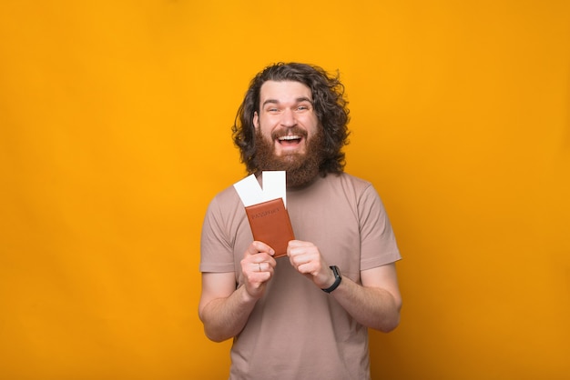 Hombre hipster barbudo asombrado con pelo largo y rizado mostrando pasaporte y boletos