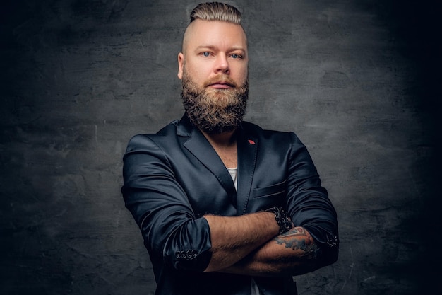 Un hombre hipster barbudo con brazos cruzados tatuados, vestido con una chaqueta violeta sobre fondo de viñeta gris.