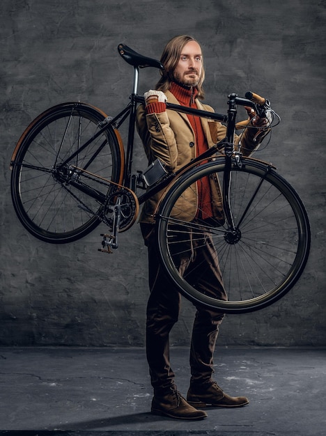 Foto hombre hipster barbudo casual sostiene con bicicleta de una sola velocidad sobre fondo gris.