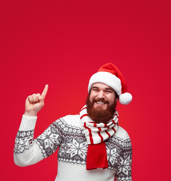 Hombre hipster barbudo con sombrero de santa apuntando hacia arriba