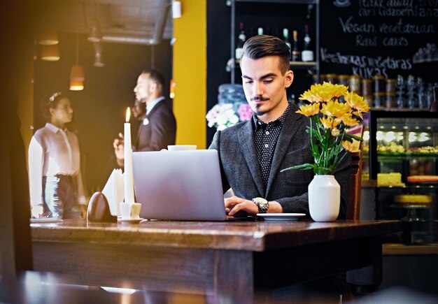 Un hombre hipster de bigote serio usando una laptop en un café.