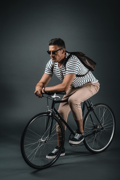 Hombre hipster con estilo apoyado en bicicleta aislado en gris