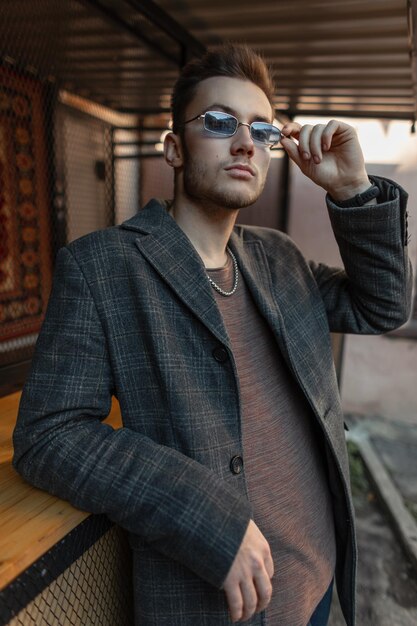 Un hombre hipster a la moda con ropa informal y un elegante abrigo lleva gafas de sol en la calle