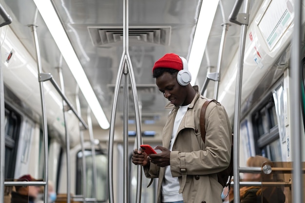 Hombre hipster negro usa auriculares inalámbricos escuchando música usando un teléfono inteligente en el tren subterráneo