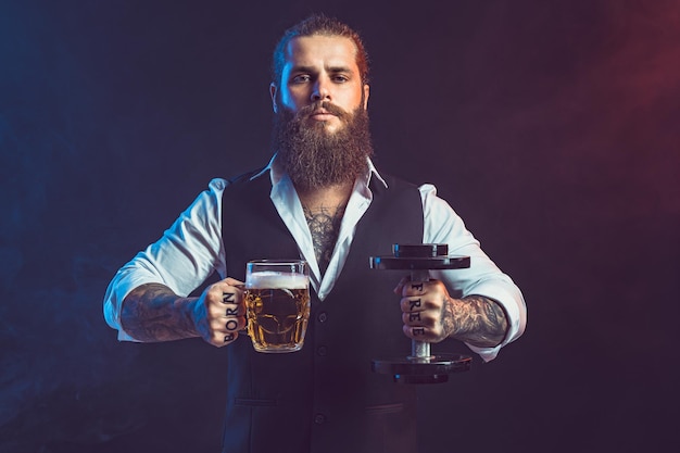 El hombre hipster sostiene una pesa y una jarra de cerveza en las manos concepto de elección entre alcohol y deporte