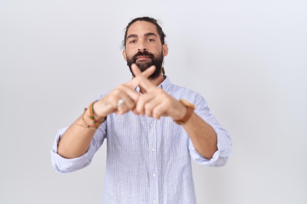 Hombre hispano con barba con expresión de rechazo de camisa casual cruzando los dedos haciendo señal negativa