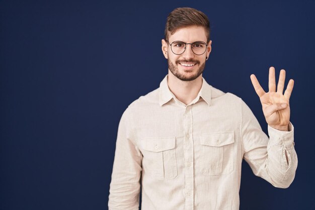 Hombre hispano con barba sobre fondo azul que aparece y señala con los dedos número cuatro mientras sonríe confiado y feliz.