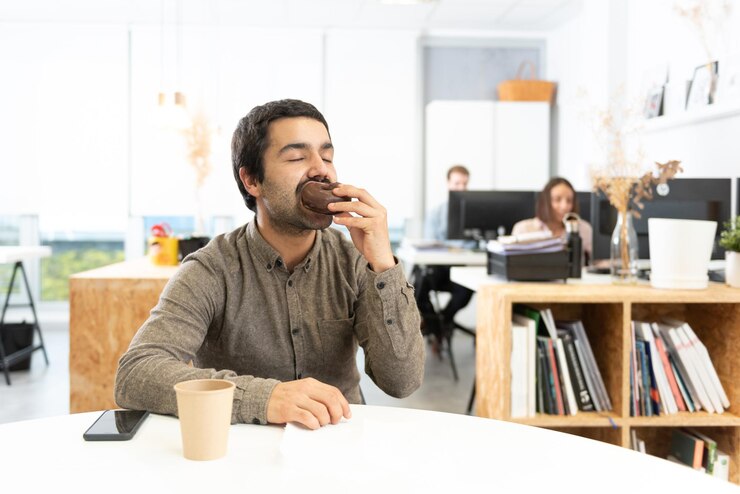 Hombre hispano comiendo y disfrutando de un bollo dulce de chocolate Hábitos poco saludables en el concepto de oficina