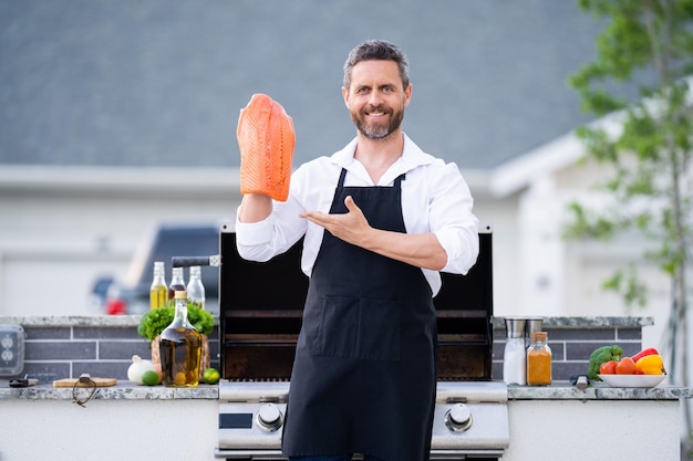 Hombre hispano en delantal de cocinero cocinando salmón a la parrilla en el patio trasero de la casa