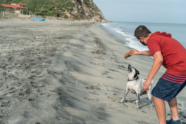 Hombre hispano divirtiéndose con su perro en la playa