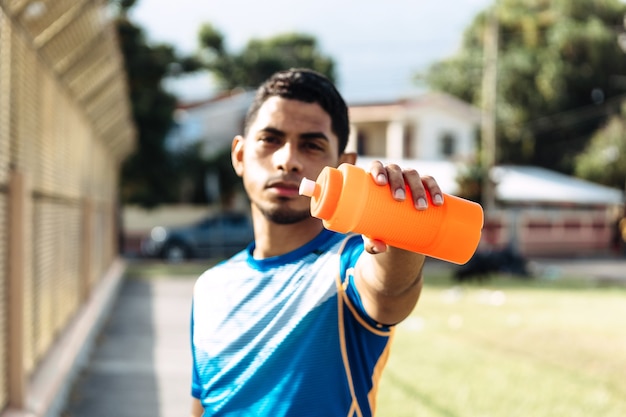 Hombre hispano de fitness desenfocado sosteniendo una botella de plástico beber sin bpa
