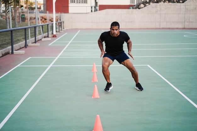 Hombre hispano haciendo ejercicios de cono de velocidad y agilidad sesión de entrenamiento al aire libre