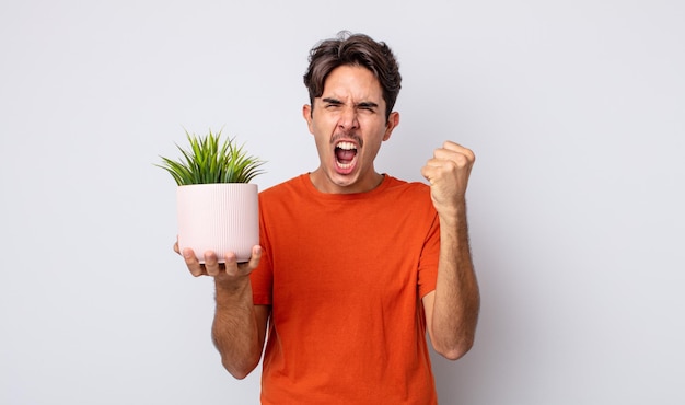 Hombre hispano joven que grita agresivamente con una expresión enojada. concepto de planta decorativa