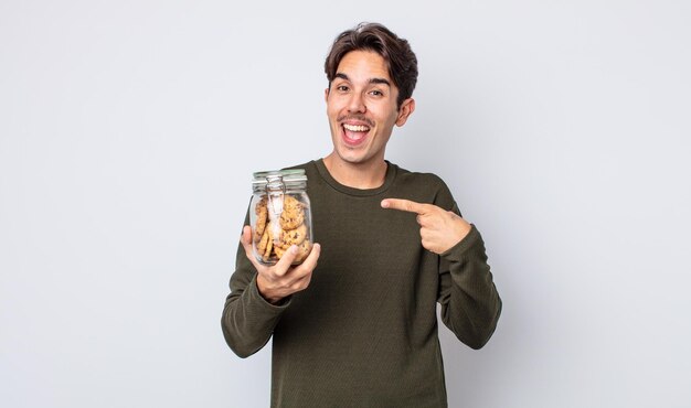 Hombre hispano joven que parece emocionado y sorprendido apuntando hacia el lado. concepto de cookies