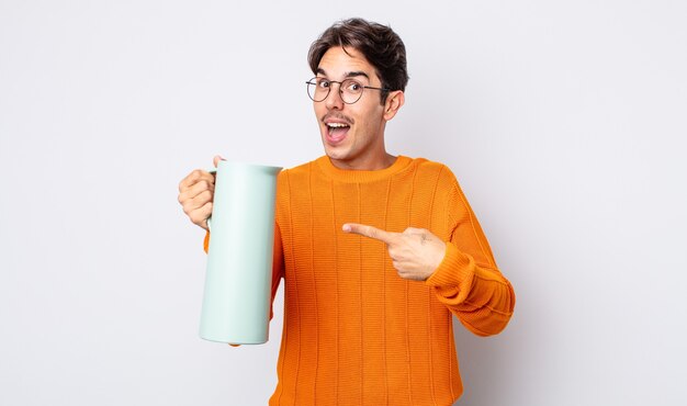 Hombre hispano joven que parece emocionado y sorprendido apuntando hacia el lado. concepto de termo