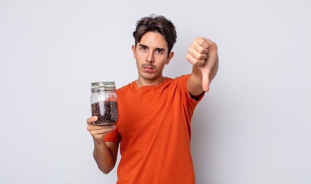 Foto hombre hispano joven que se siente cruzado, mostrando los pulgares hacia abajo. concepto de granos de cafe