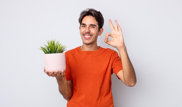 Hombre hispano joven que se siente feliz, mostrando aprobación con gesto bien. concepto de planta decorativa